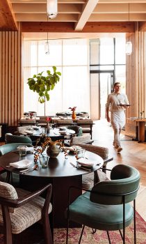 Eclectic dining room with round tables, padded chairs and various painted vases. A server walks by tables carrying a tray.