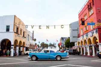 A vintage car passes a crossroad beneath a suspended 